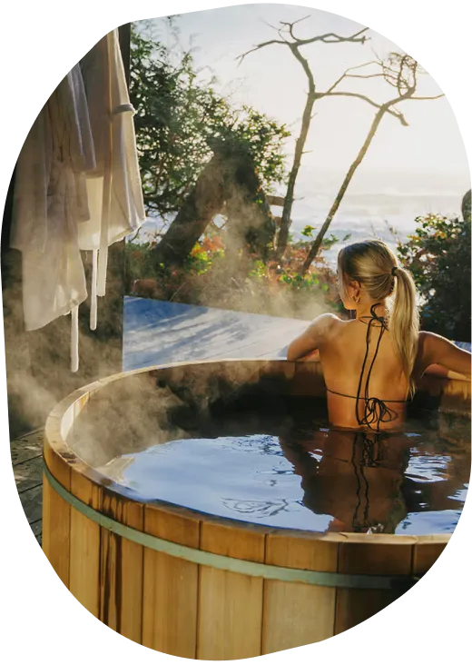 Female in round cedar hot tub overlooking forest and ocean
